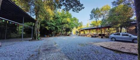 A gravel pathway leading to covered structures, a parked car, and trees in a park-like setting.