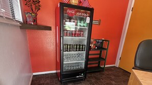 A Coca-Cola refrigerator with American flags, a shelf with decorative items, and a chair. - Historic Mora Inn and RV Park (Cleveland)