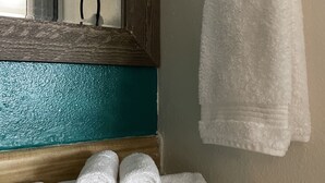 A bathroom with a wooden vanity, a mirror, a towel rack with a white towel, and three bottles of Terra Pure body care products. - Historic Mora Inn and RV Park (Cleveland)