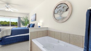 A bedroom with a large bed, a bathtub, and a balcony with a view of trees.