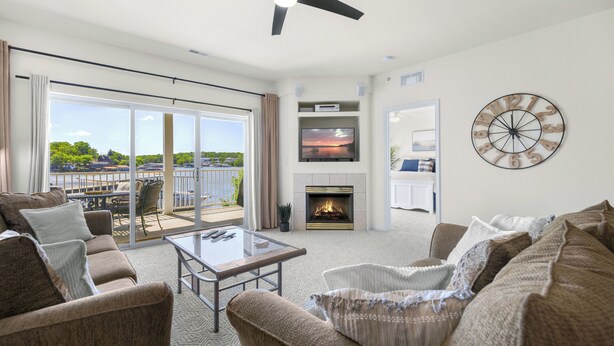 A spacious living room with a fireplace, comfortable seating, a large window with a view, and a ceiling fan.