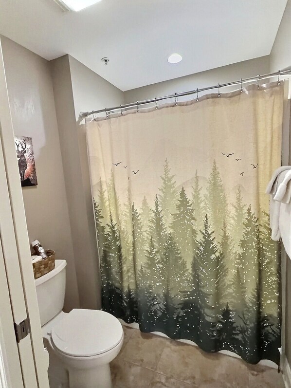 A bathroom with a toilet, a shower curtain depicting a forest scene, and a towel hanging on the wall.
