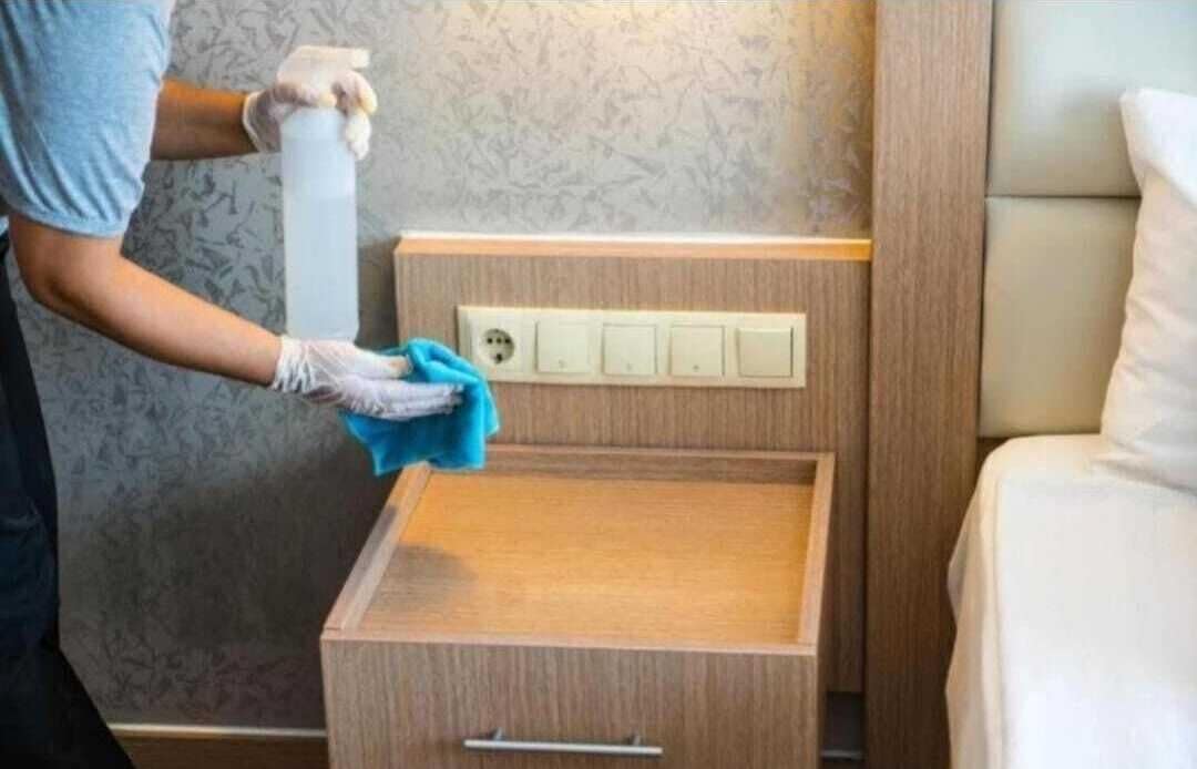 A person cleaning a wooden drawer unit in a hotel room.