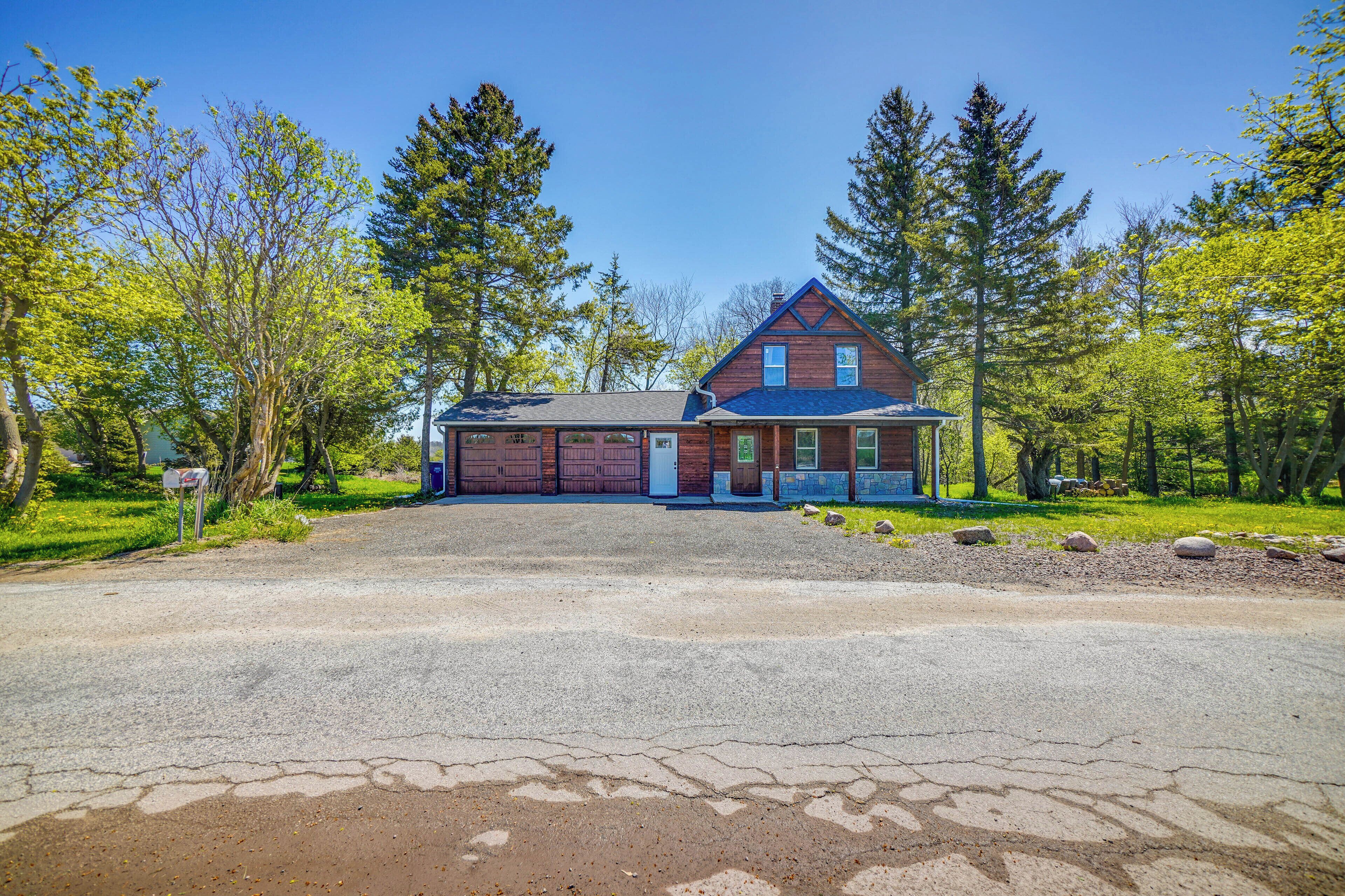 A two-story house with a garage, surrounded by trees and a gravel driveway.