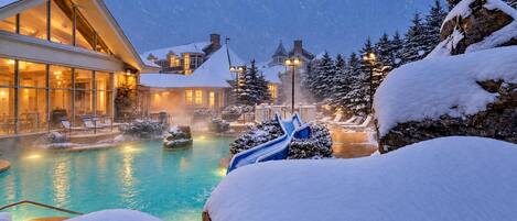A resort with a heated pool, lounge chairs, and snow-covered trees.