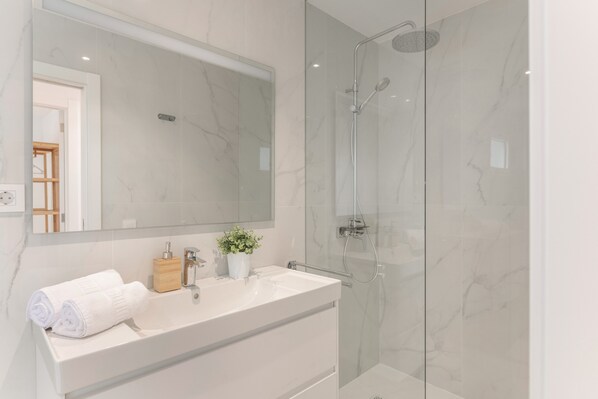 A modern bathroom with a glass-enclosed shower, a white vanity with a mirror, and a potted plant.