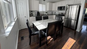 A modern kitchen with white cabinets, a stainless steel refrigerator, a built-in oven, and a dining area with a marble table and leather chairs.