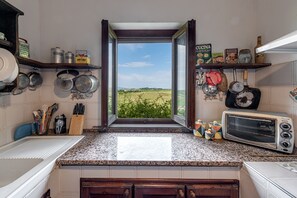 A kitchen with a view of a field, a microwave, and various kitchen utensils.