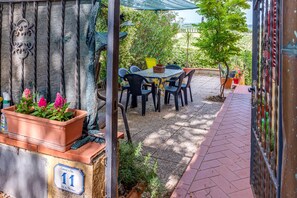 Une terrasse extérieure avec une table et des chaises, entourée de plantes en pot et d’une clôture décorative en métal.