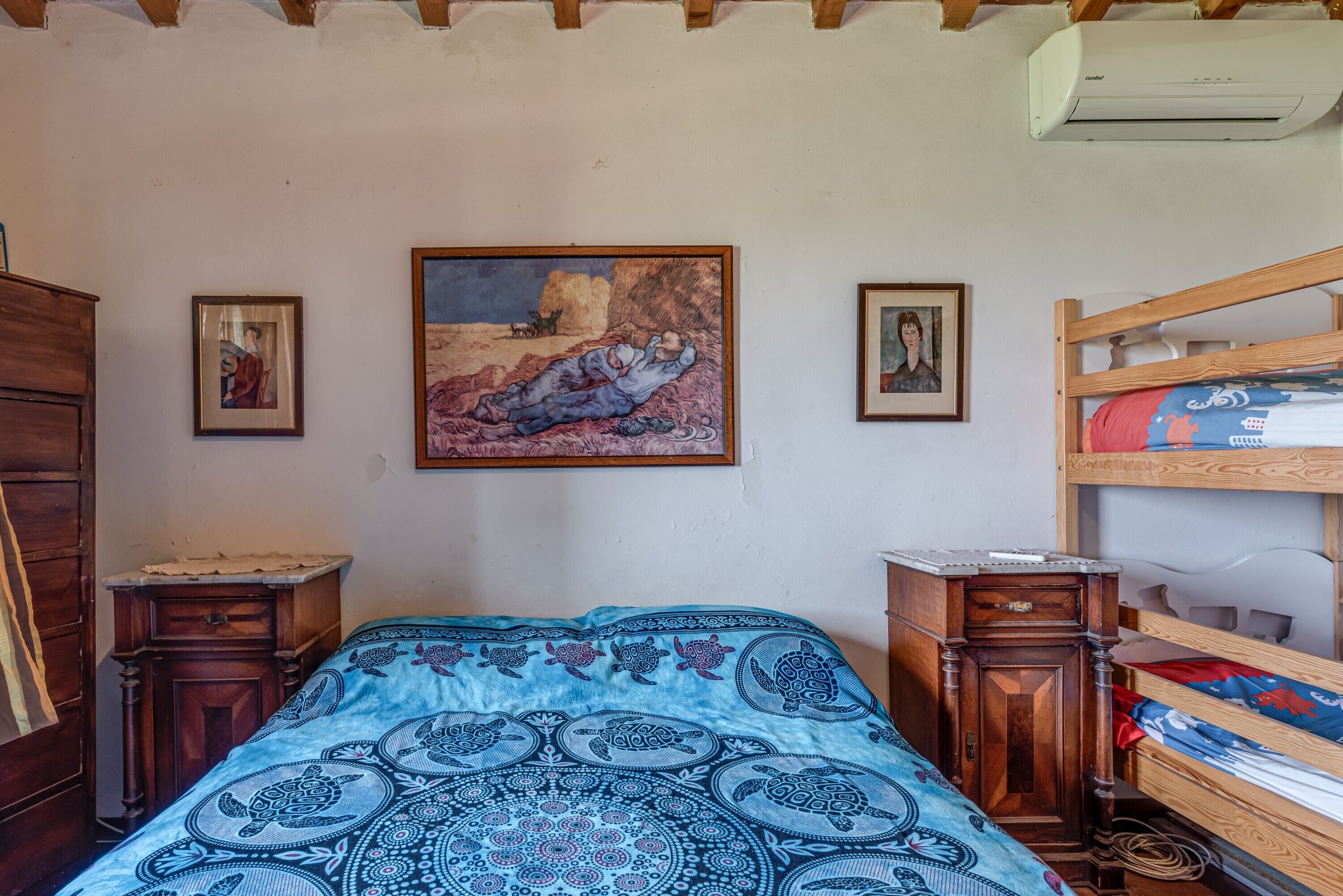 Una camera da letto con una coperta a motivi, un quadro appeso al muro, un comò di legno e un letto a castello.