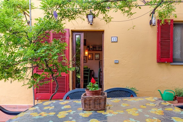 An outdoor seating area with a table, chairs, a potted plant, and a building entrance.