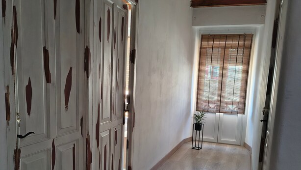 Un pasillo con pisos de madera, paredes blancas y una ventana con persianas.