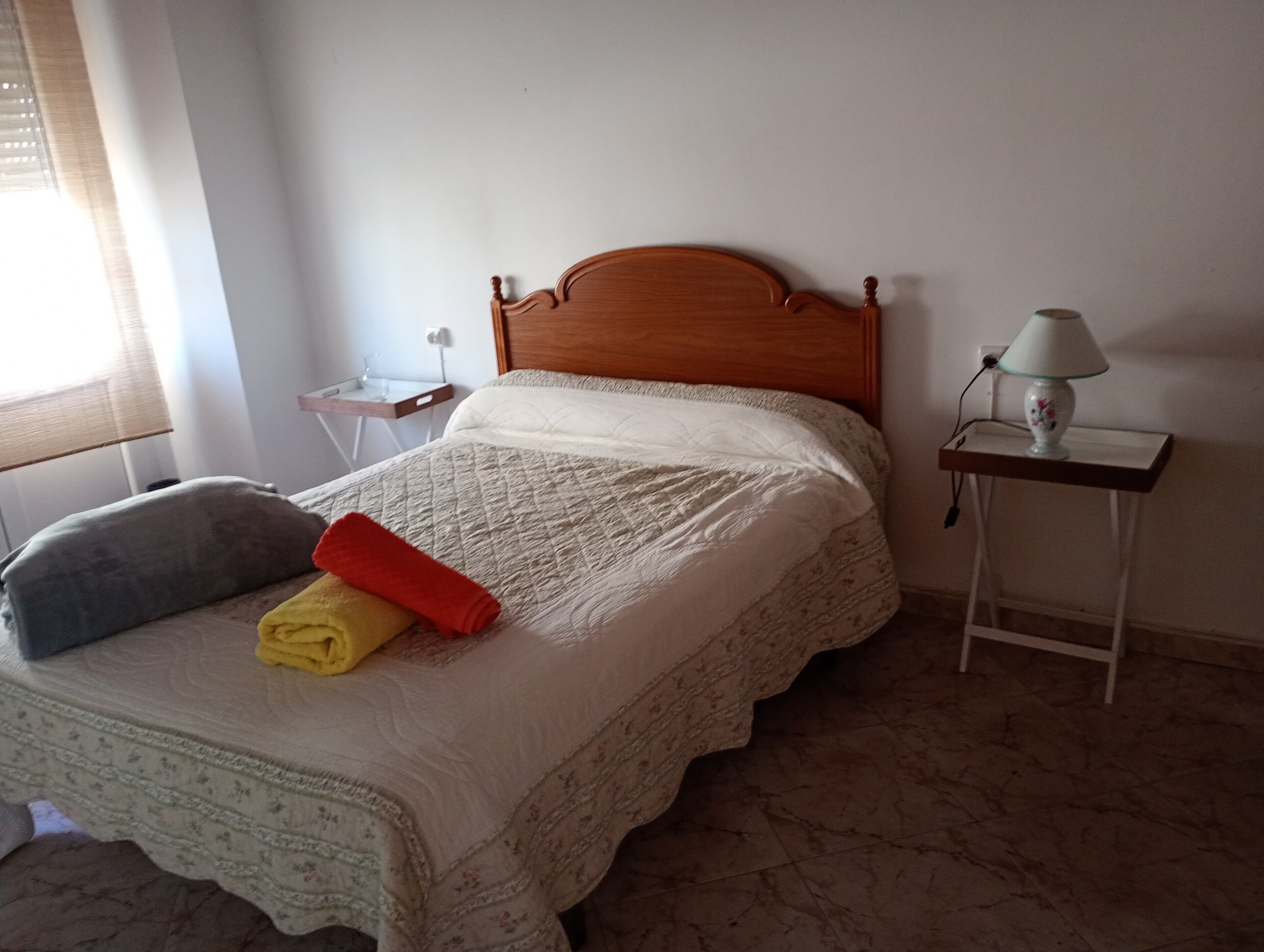 Un lit avec une tête de lit en bois, une table de chevet avec une lampe et une fenêtre avec des stores.