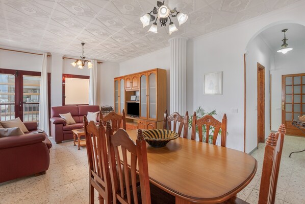 Un comedor con mesa y sillas de madera, un televisor y un aparador con puertas de vidrio.
