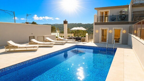 A swimming pool with lounge chairs, a clear sky, and a building with balconies.