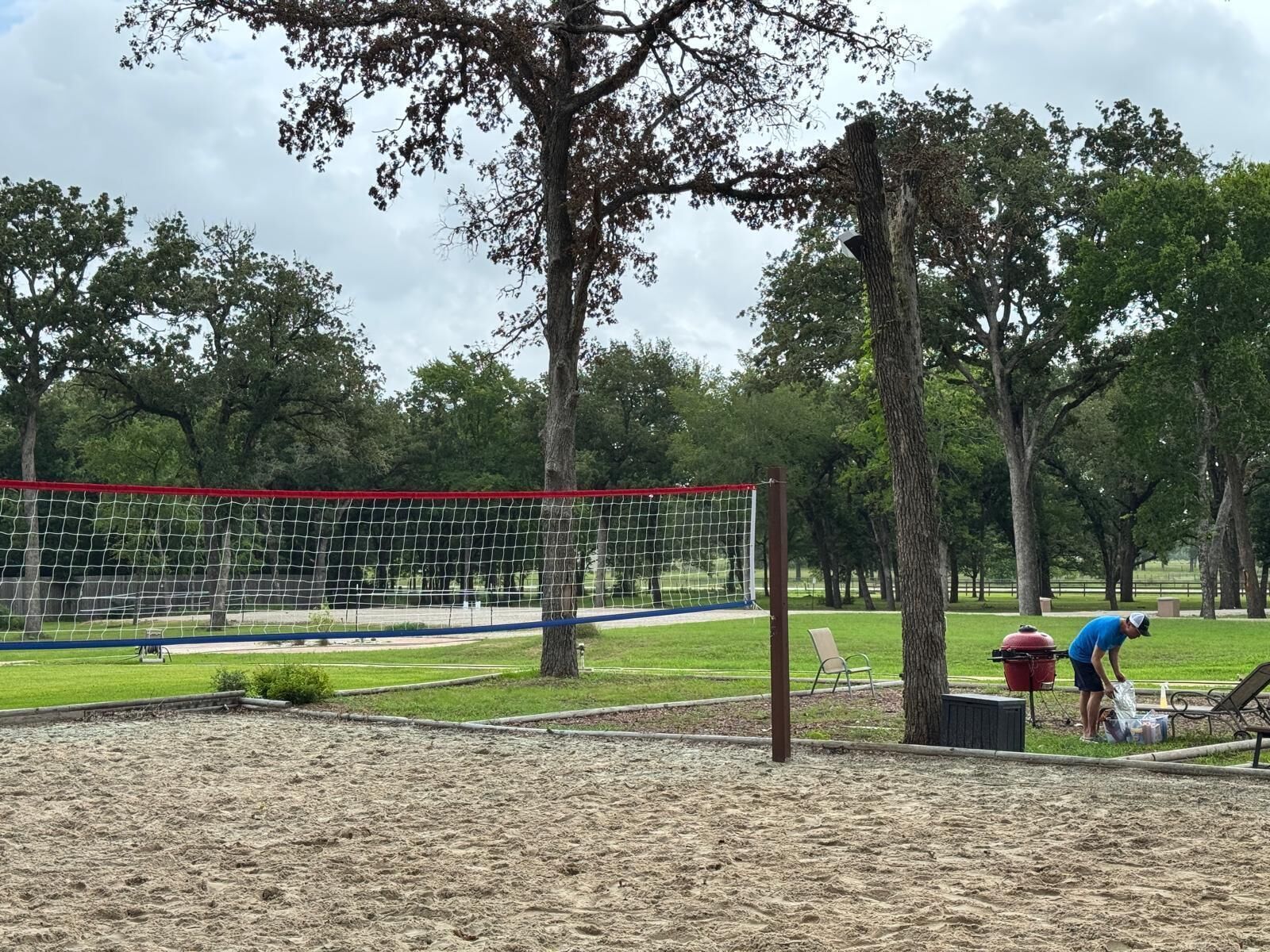 A sandy volleyball court with a net, surrounded by trees and a grassy area.