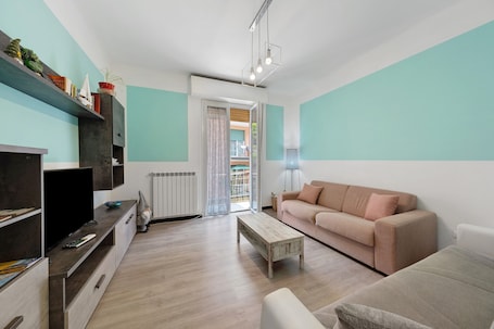 A modern living room with a sofa, coffee table, TV, and shelves with decorative items.
