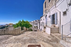 A narrow street with buildings, a stone wall, and a view of the sea.