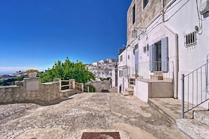 Une rue étroite bordée d’immeubles, avec un mur de pierre et une vue sur la mer.