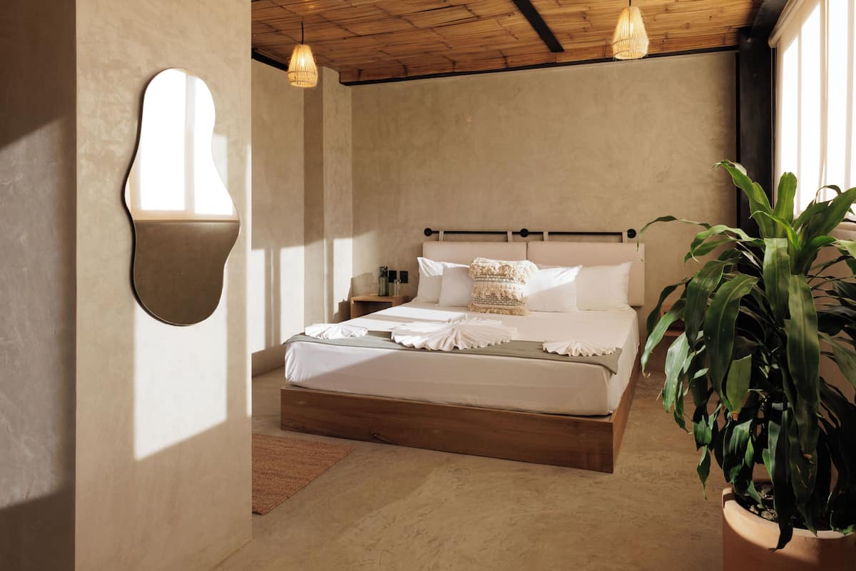 Una camera da letto con un letto con struttura in legno, un comodino, una lampada a sospensione e una pianta in vaso.