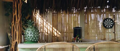 A room with a thatched roof, wicker chairs, a dartboard, and a pineapple decoration.