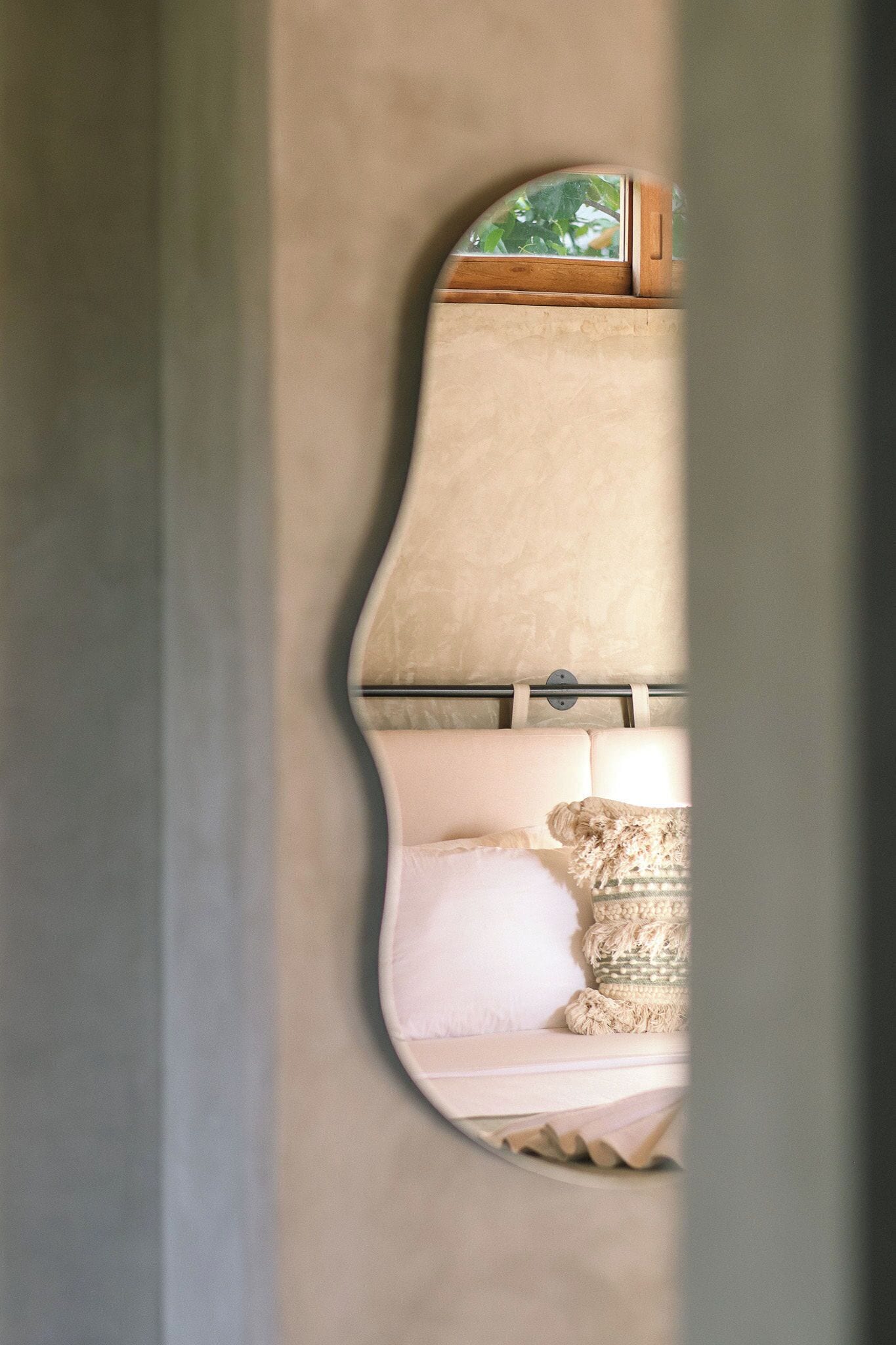 A room with a curved mirror, a white sofa, and a patterned throw pillow.