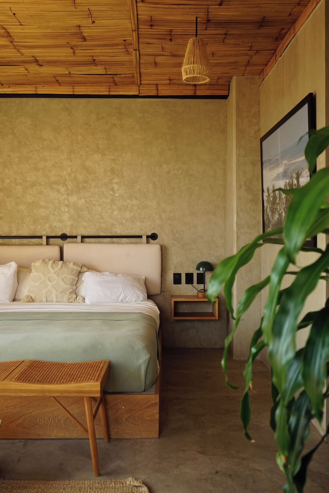 A bedroom with a wooden ceiling, a bed with white linens, a bedside table with a lamp, and a framed picture on the wall.