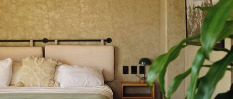 A bedroom with a wooden ceiling, a bed with white linens, a bedside table with a lamp, and a framed picture on the wall.