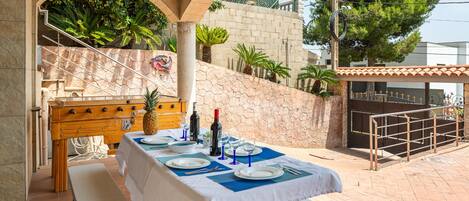 An outdoor dining area with a table set for four, a wooden bench, and a stone wall with plants.
