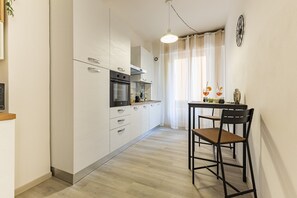 Une cuisine compacte dotée d’un four encastré, d’une table à manger avec des chaises et d’un luminaire suspendu.