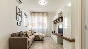 A modern living room with a sofa, a TV, and a kitchen area with a refrigerator.