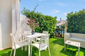 A patio with a white table and chairs, a small white table with a bowl and a plate, and a white sofa.