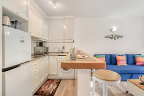 A compact kitchen with a microwave, sink, and a wooden island. There is a washing machine and a blue sofa in the living area.