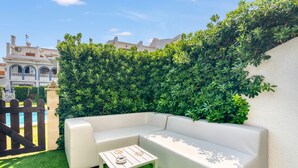 Uma área de estar ao ar livre com mesas, rodeada por vegetação exuberante e uma piscina ao fundo.