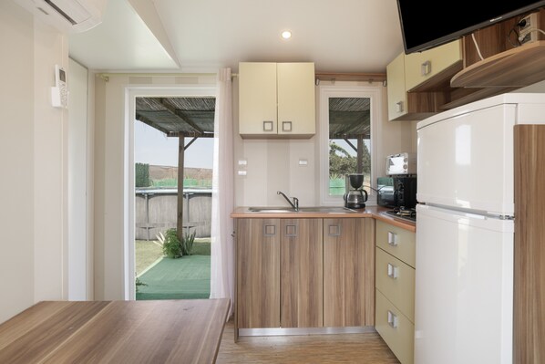 A compact kitchen with wooden cabinets, a built-in sink, and a white refrigerator. - Mobile Home 'Isabella' with Private Pool, Private Terrace and Private Garden (Conil de la Frontera)