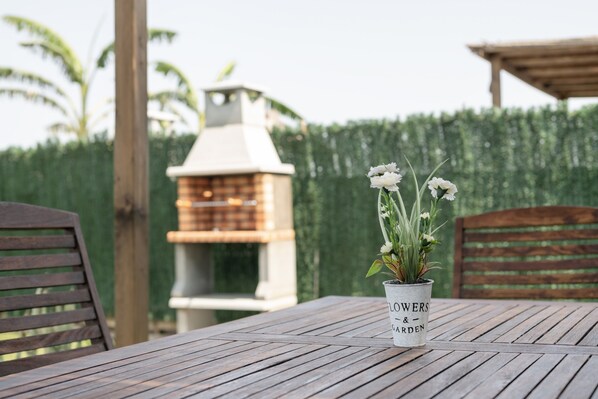Una mesa de madera con una planta en maceta, una parrilla y una silla de madera.