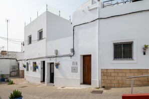 A white building with a wooden door, a window with metal bars, and a potted plant on the wall. - Apartment 'Boquerón' with Sea Views, Private Terrace and Wi-Fi (Conil de la Frontera)