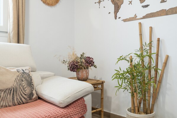 Une pièce avec un canapé blanc, un coussin à motifs zébrés, une petite table sur laquelle est posée une plante en pot et une carte géographique accrochée au mur.