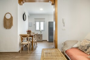 Une pièce comprenant un lit, une table à manger avec des chaises, un coin cuisine et une horloge fixée au mur.