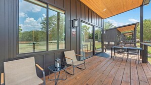 A covered outdoor seating area with tables and chairs, large windows, and a view of the park.