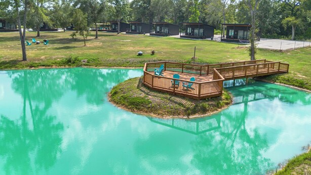A resort with a central wooden deck surrounded by turquoise water, connected to a larger area by a wooden bridge.