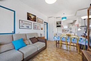 A living room with a sofa, a dining table with chairs, and a kitchen area in the background.