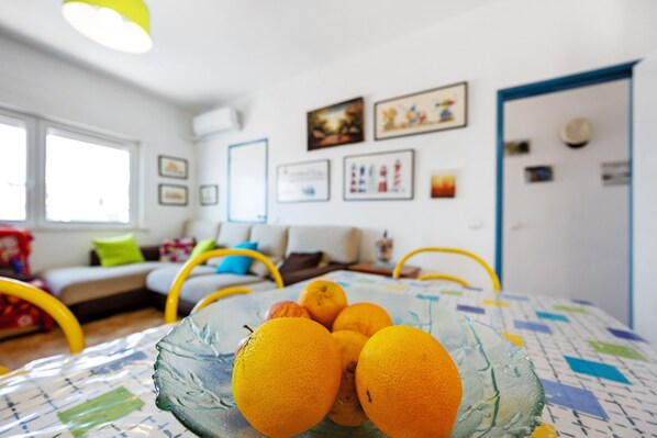 A dining table with a glass bowl of oranges, a sofa, and a door in a room with framed pictures on the wall.