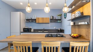 Uma cozinha moderna com ilha central, cadeiras de madeira, luminárias pendentes e prateleiras embutidas.