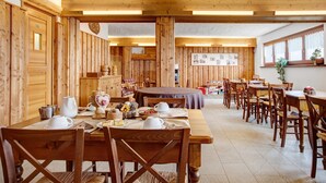 Un intérieur en bois avec plusieurs tables et chaises, des murs en bois et une horloge au mur.