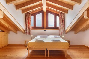 Une pièce avec un plafond en bois, un lit avec deux oreillers, une table de chevet et une fenêtre avec des rideaux.