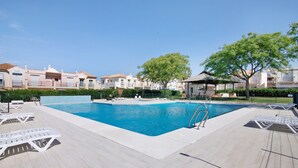 A swimming pool with lounge chairs, a clear sky, and residential buildings in the background. - Holiday Home 'Estrella' with Mountain View, Wi-Fi and Air Conditioning (ayamonte)