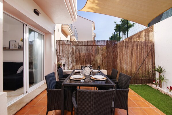 A patio with a table set for four, surrounded by wicker chairs, a sliding glass door, and a bamboo fence. - Holiday Home 'Estrella' with Mountain View, Wi-Fi and Air Conditioning (ayamonte)