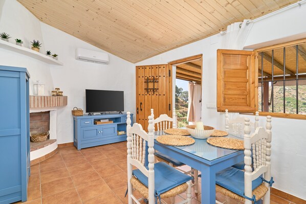 Un comedor con mesa azul y sillas blancas, televisor y chimenea.
