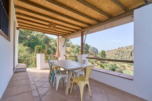 An outdoor patio with a table and chairs, a pergola, and a view of a hilly landscape.